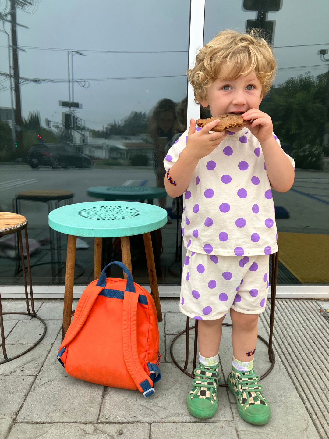 A child eating a cookie, wearing a kids' tee shirt and shorts set in a pattern of purple dots on an ecru background