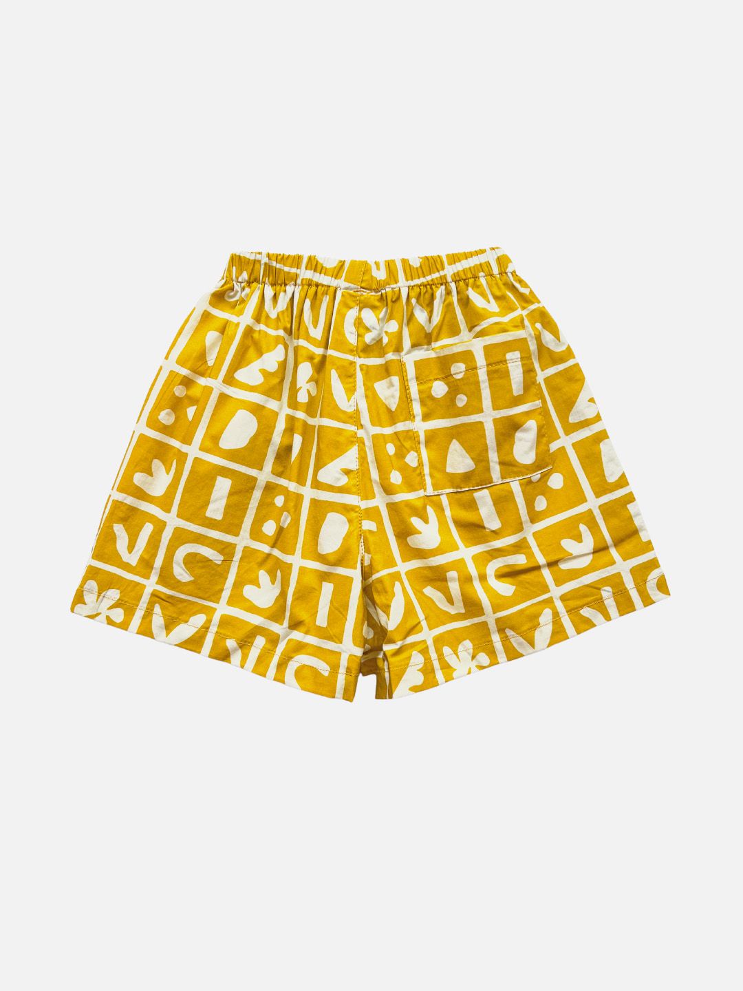 A pair of kids' shorts in mustard yellow, overlaid with a grid of different shapes in white, with back pocket, rear view