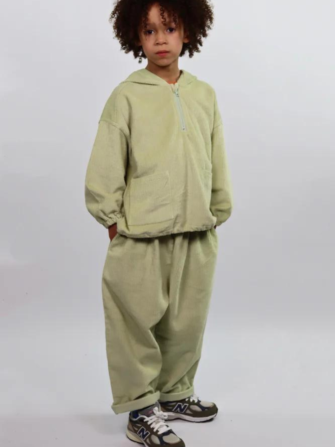 A child wearing a matching kids' hooded smock top and pants in light pistachio green