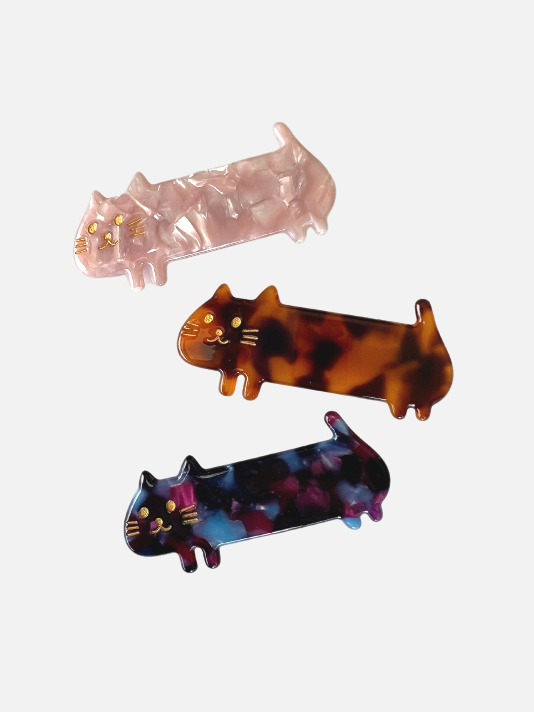 Three kids' barrettes in the shape of elongated cats: one pink, one ginger, one purple