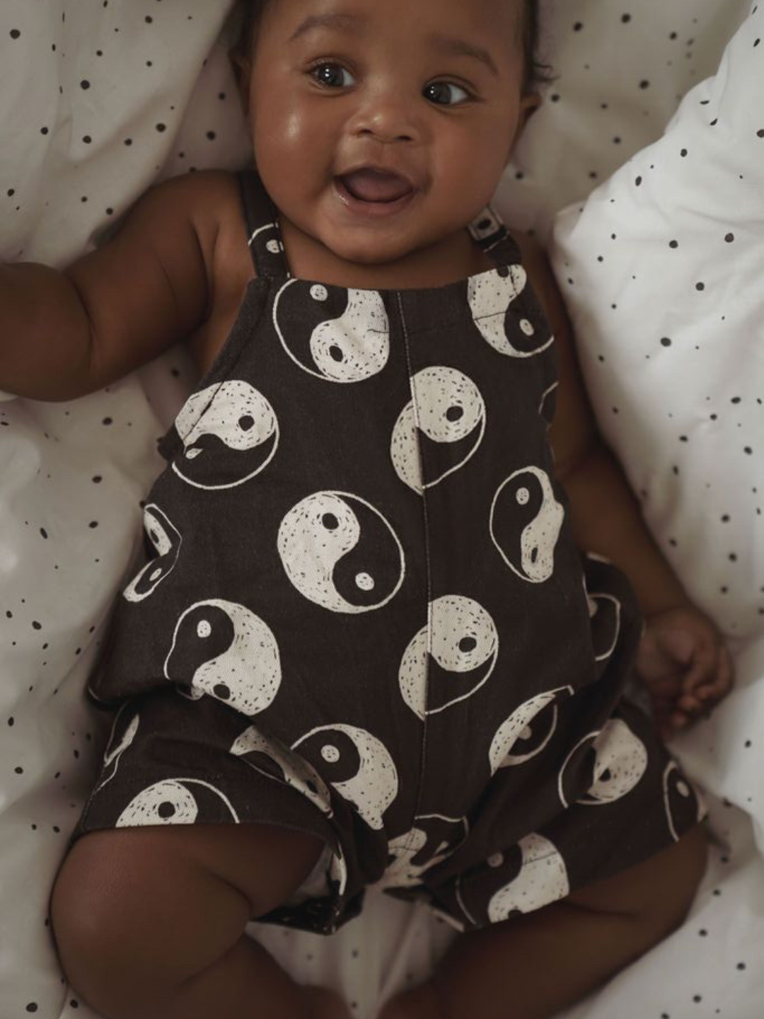 A front view of black overalls with a yin and yang pattern all over on a child.