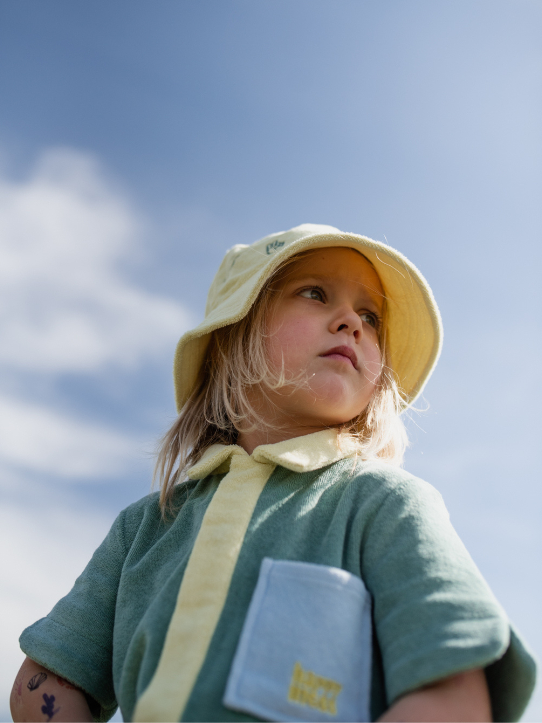 Cactus | A child wearing a pale green kids' jumpsuit with yellow collar and placket, and blue pockets