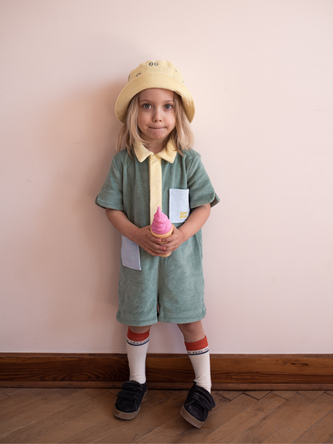 Cactus | A child wearing a pale green kids' jumpsuit with yellow collar and placket, and two blue pockets