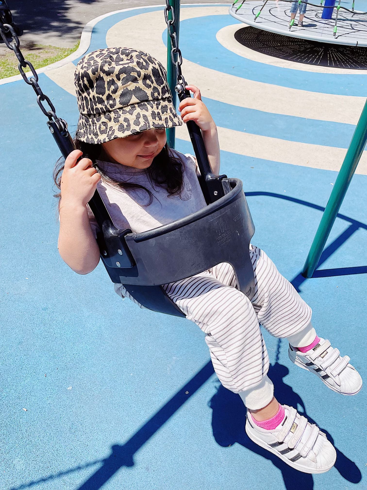 A child on a swing in a kids' leopard print bucket hat