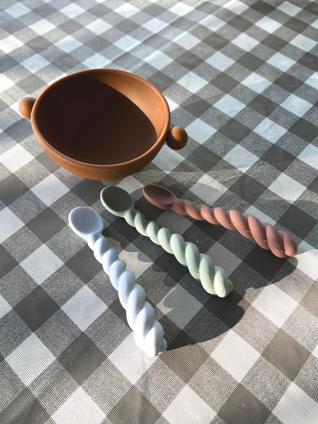 Three rubber kids spoons on table cloth next to a bowl