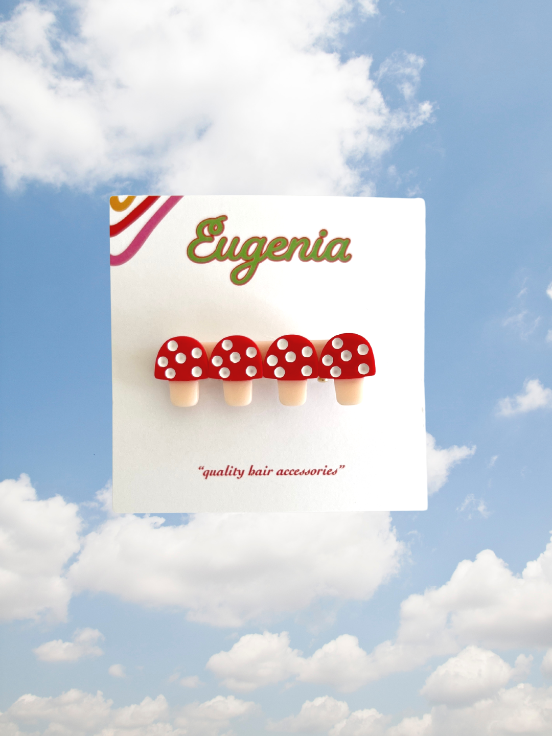 A presentation card of a kids' hair clip featuring four red toadstools with white spots