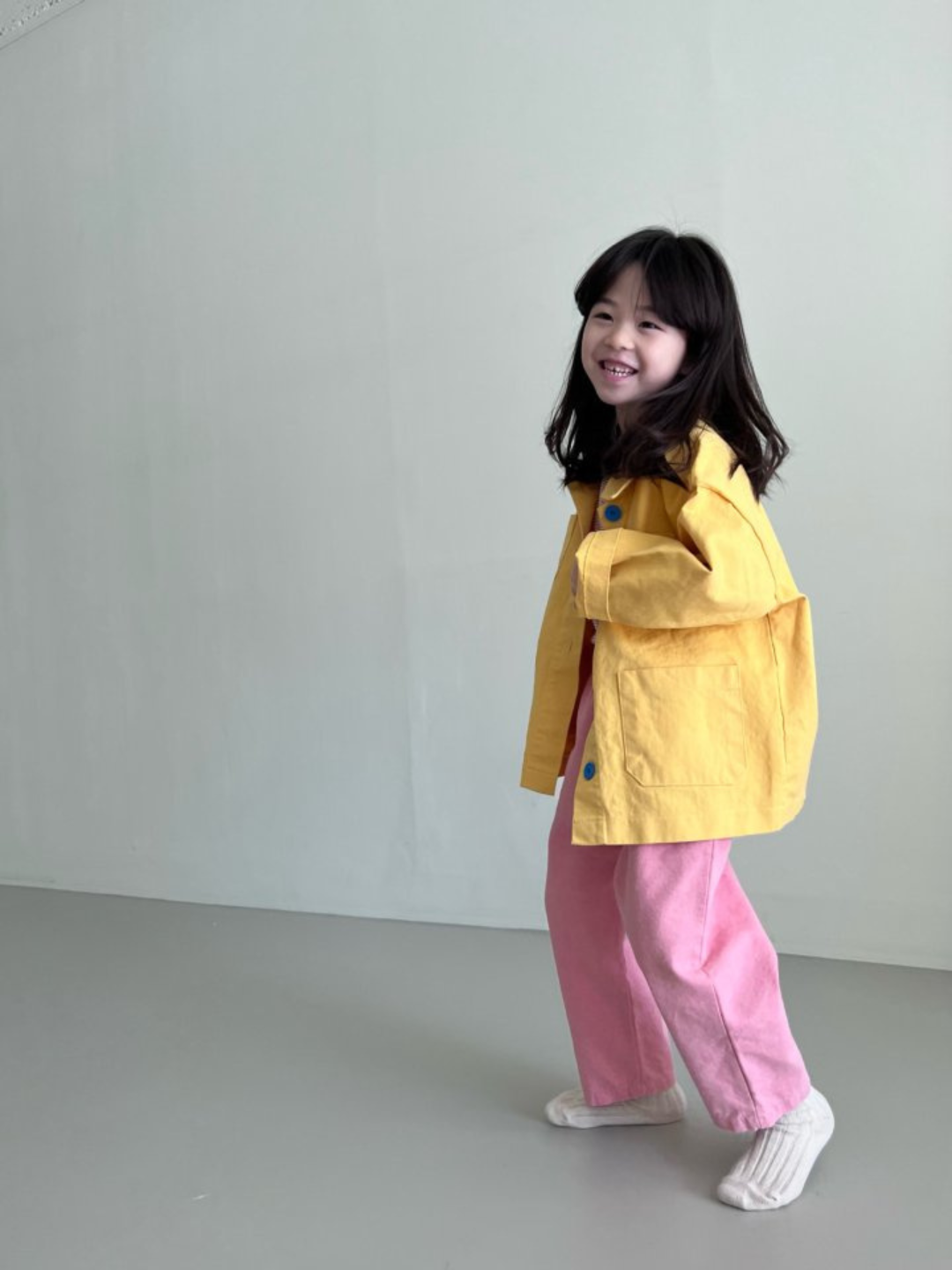 A child wearing a kids' jacket in yellow, with four pockets and four blue buttons