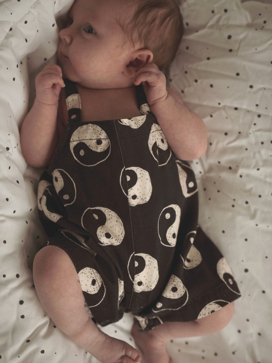 A front view of black overalls with a yin and yang pattern all over on a baby.