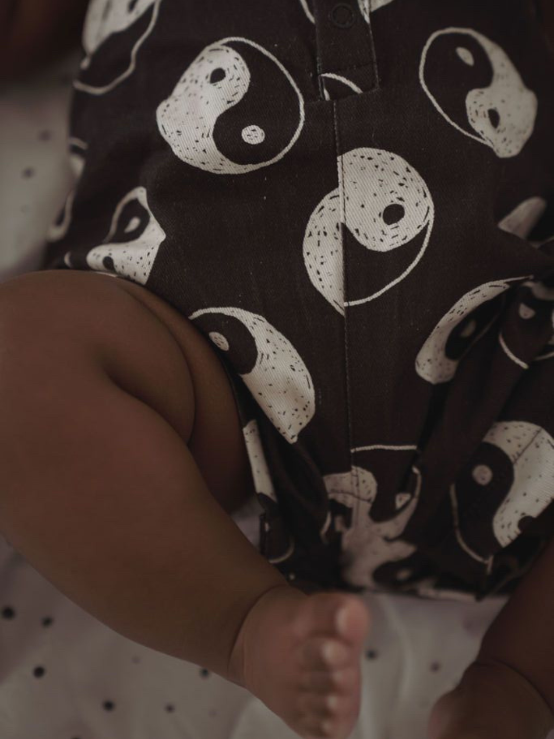 A zoomed in front view of black overalls with a yin and yang pattern all over on a child.