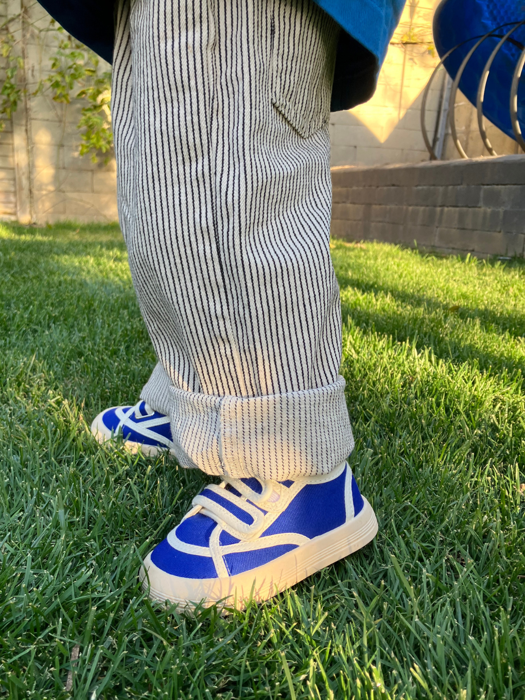 Child standing on grass wearing pair of kids' sneakers in blue with white trim