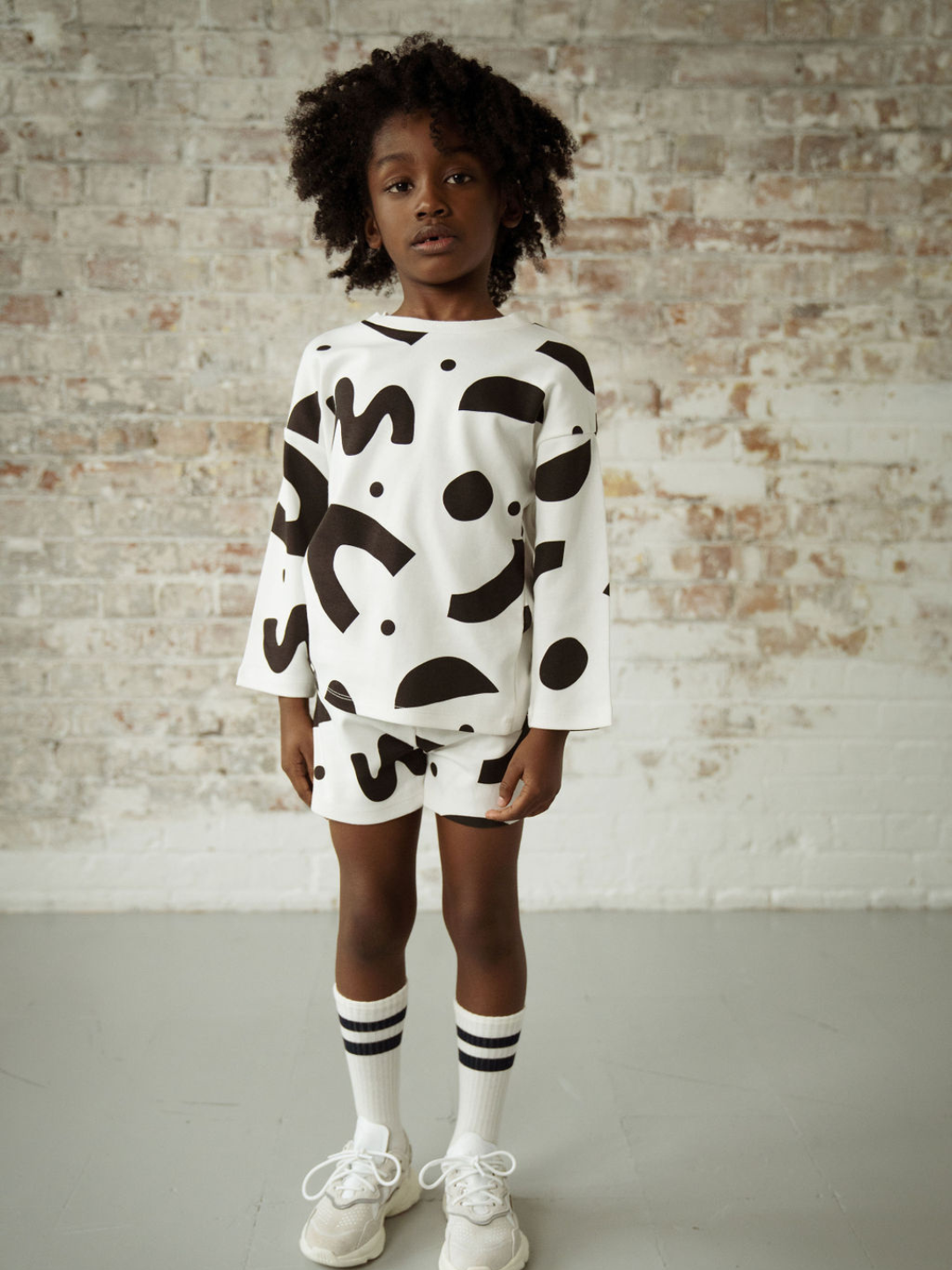 A child wearing a kids' long-sleeved tee shirt in a pattern of black squiggles and dots on a white background, with matching shorts