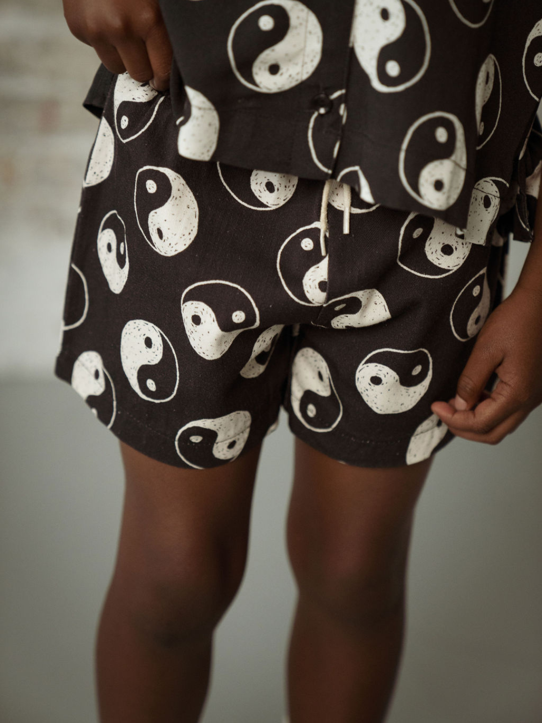 A zoomed in front view of the elastic drawstring black shorts with a yin and yang pattern all over on a child.
