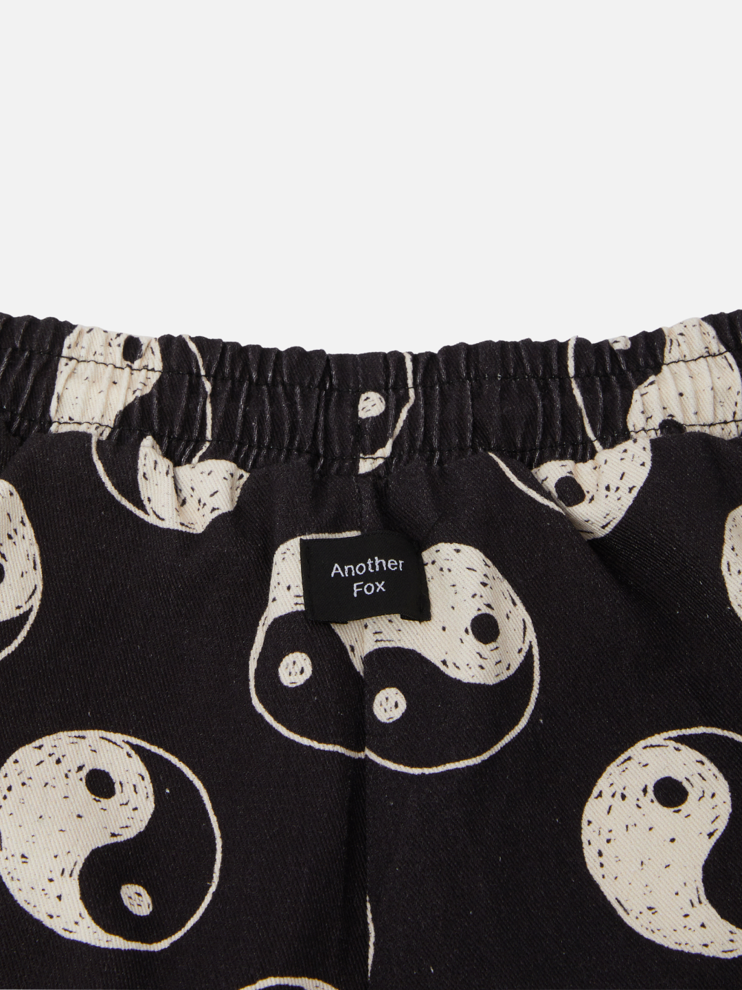 A zooming in back view of the elastic drawstring black shorts with a yin and yang pattern all over.