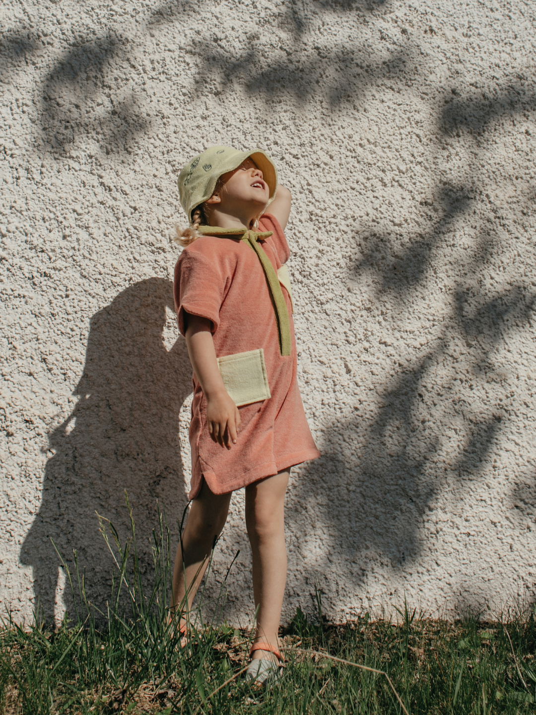 Peach | A child wearing a kids' jumpsuit in peach with lime green collar and placket, and yellow pockets