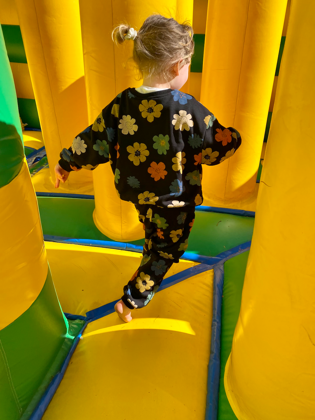 A child on a bouncy castle wearing a kids' sweatshirt and pants set in black, printed with yellow, orange, green, blue and white flowers