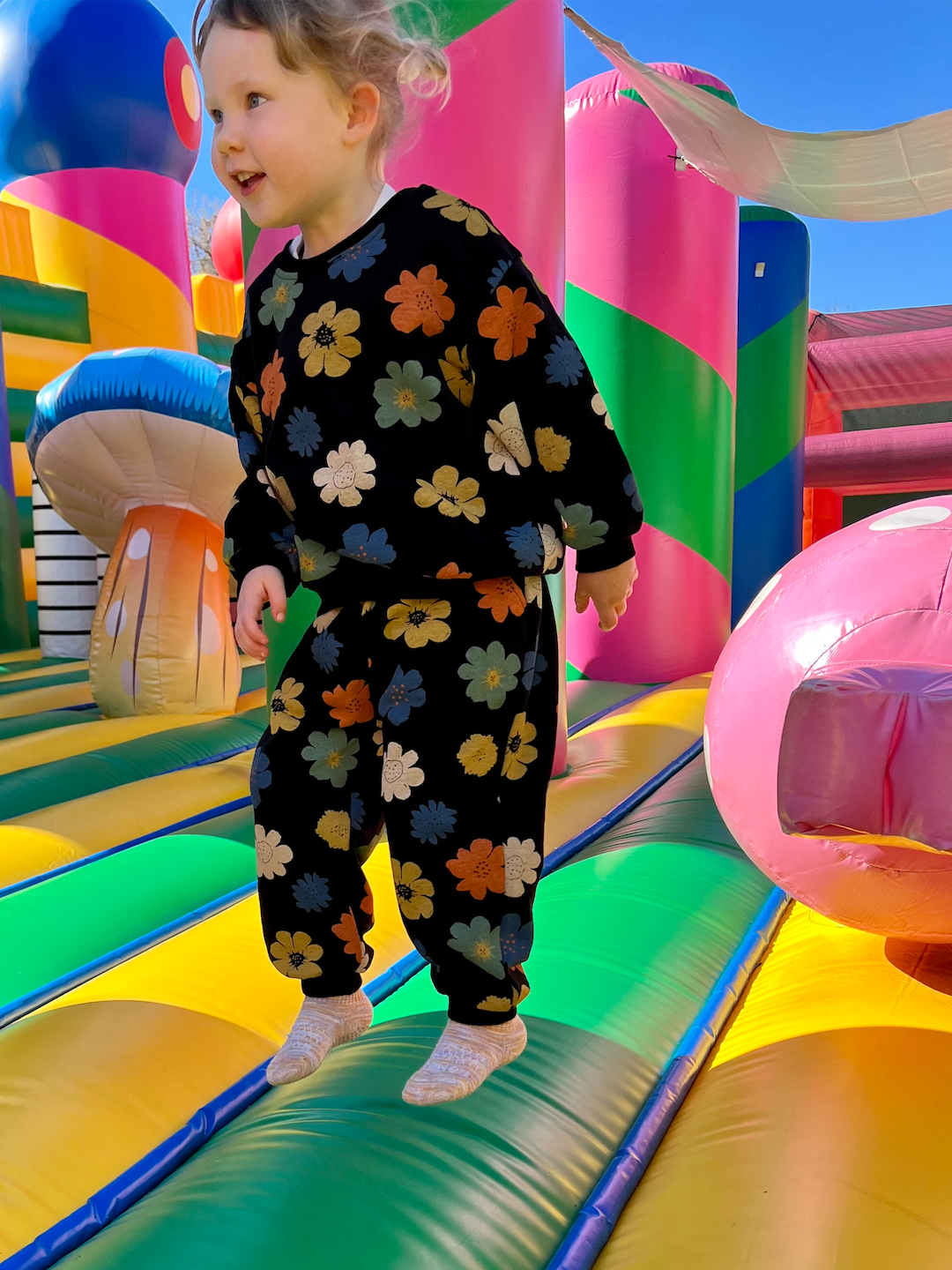 Black | A child on a bouncy castle wearing a kids' sweatshirt and pants set in black, printed with yellow, orange, green, blue and white flowers