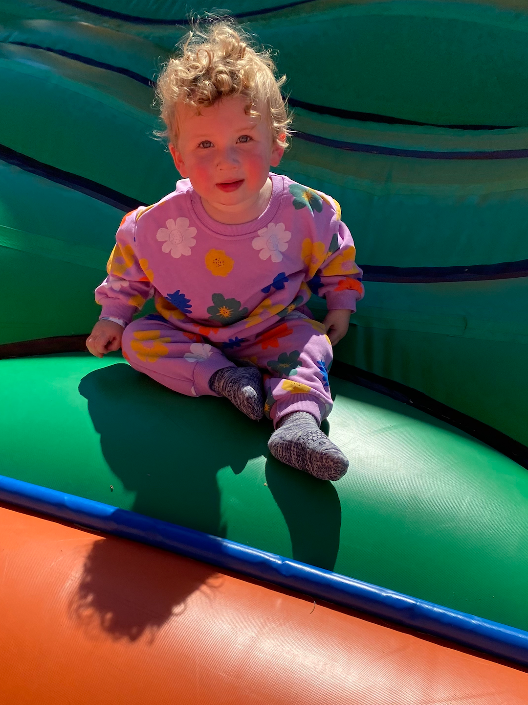 Purple | A toddler on a bouncy castle, wearing a kids' sweatshirt and pants set in purple, printed with yellow, orange, green, blue and white flowers