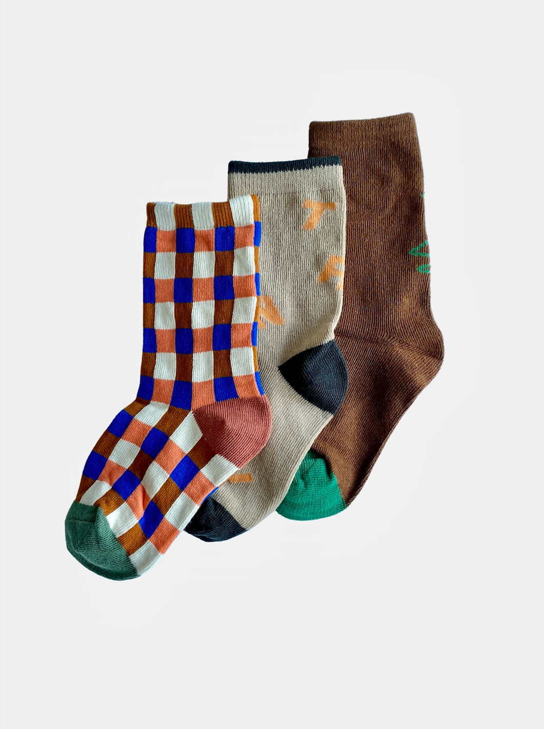 A trio of kids' ankle socks; one pair in an orange, purple and brown check with green toes; one pair in cream with yellow zigzags and black toes, heel and top; one pair in brown with green toes