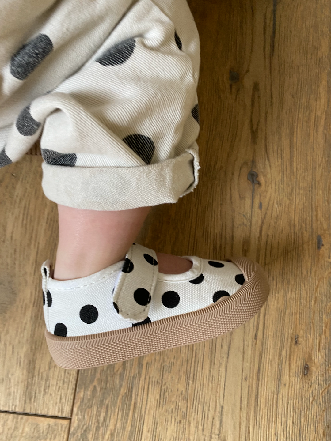A toddler wearing mary jane sneakers with black dots on a white background