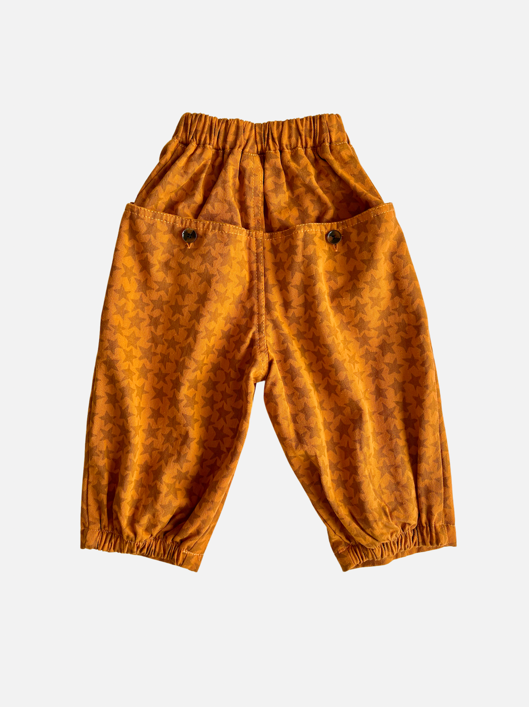 Rust | A pair of kids' pants in orange with rust star pattern and buttoned back pockets, rear view