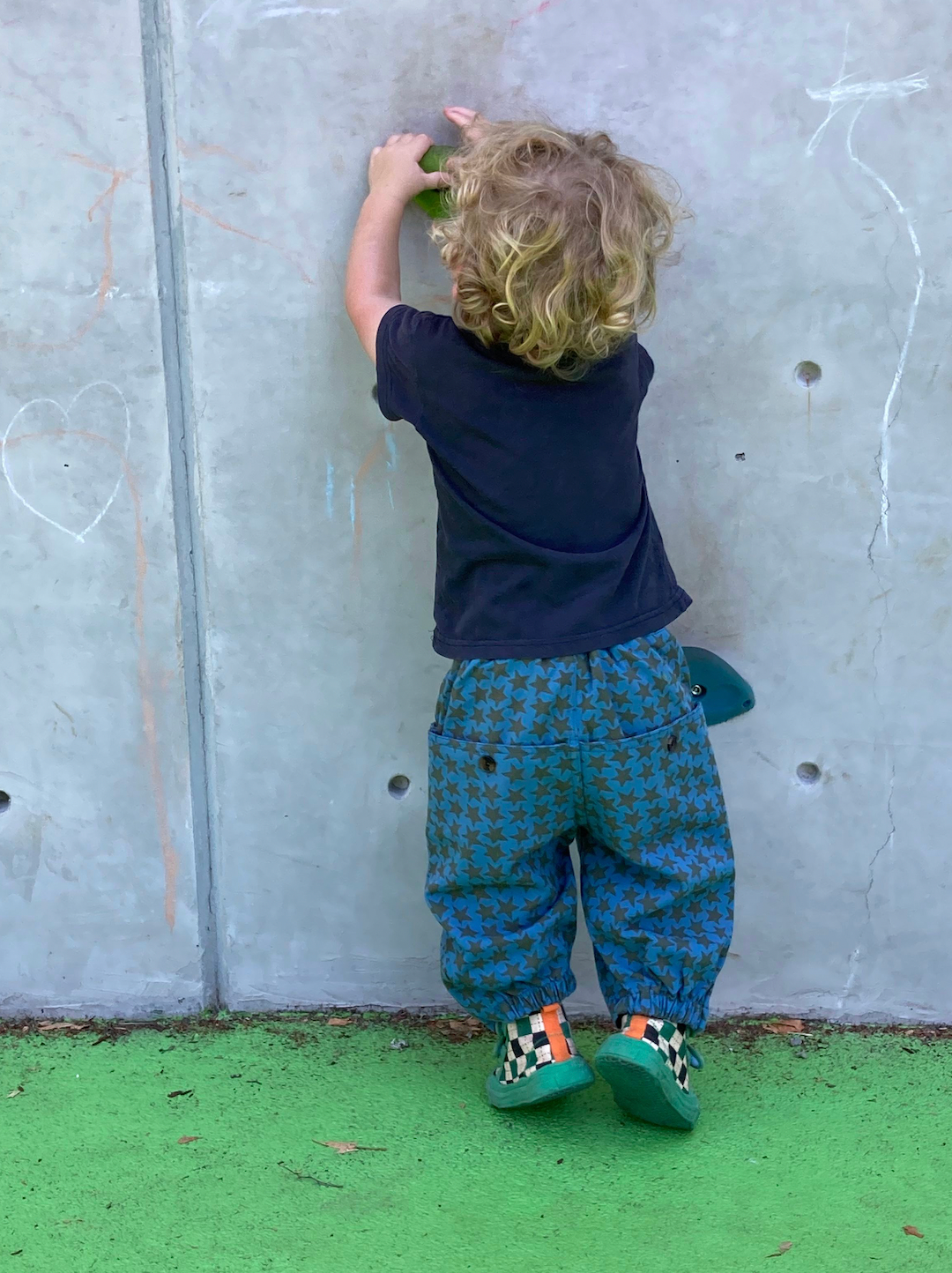 Slate | A toddler wearing a pair of kids' pants in slate blue with an olive star pattern, and buttoned back pockets