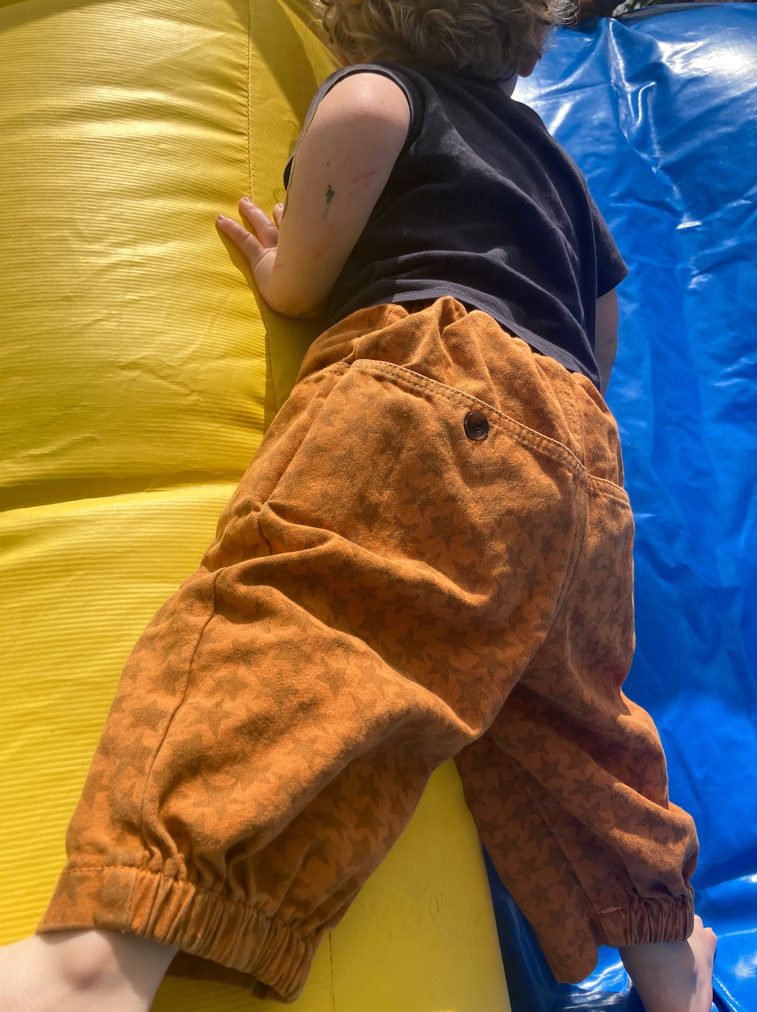 A child climbing in a pair of kids' pants in an orange and rust star pattern, with buttoned back pockets