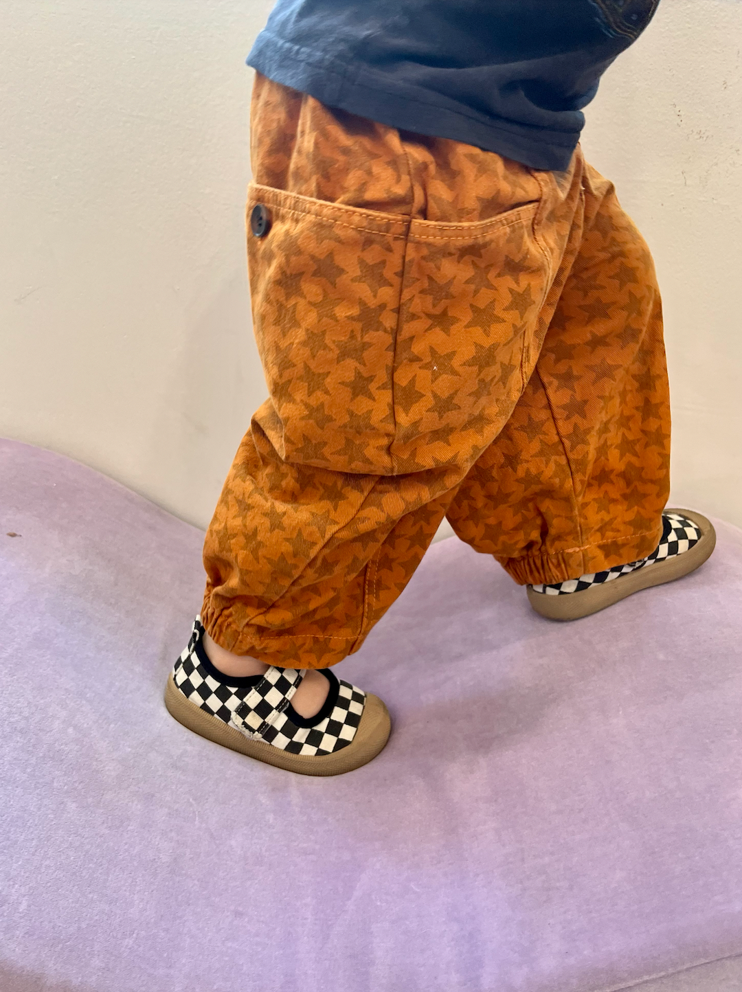 Side view of a toddler wearing kids' pants in orange with  a pattern of rust stars, showing front and back pockets