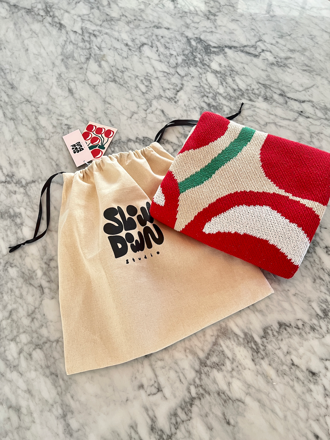 A folded mini blanket in a cherry pattern shown with its accompanying gift bag