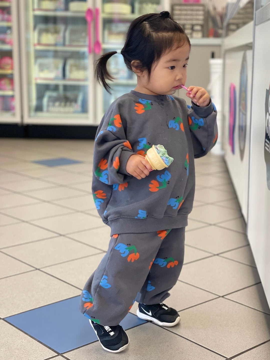 Child eating ice cream in a store, wearing kids' sweatshirt and pants in slate gray, printed with blue and orange flowers