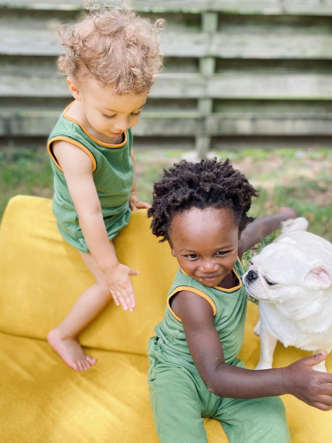 One child in mint green kids' tank and bloomers, next to child in similar tank and mint green pants, playing with dog in backyard