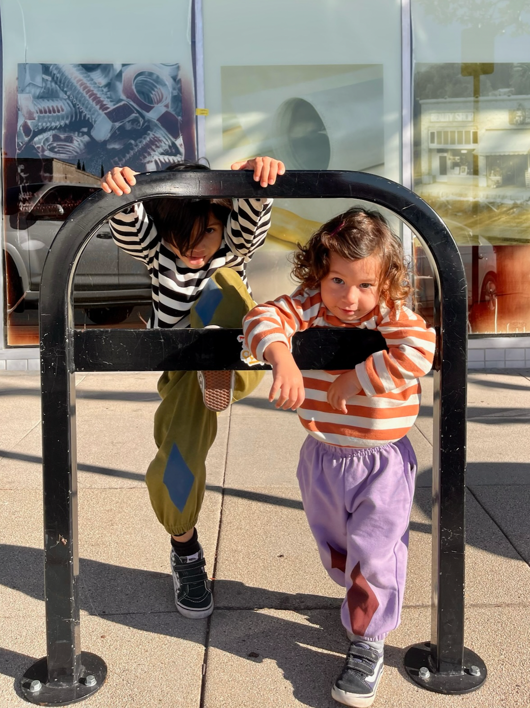 Two children wearing kids' sweatpants: one pair in olive green with blue diamond knee patches, one in pale purple with dark red diamond patches