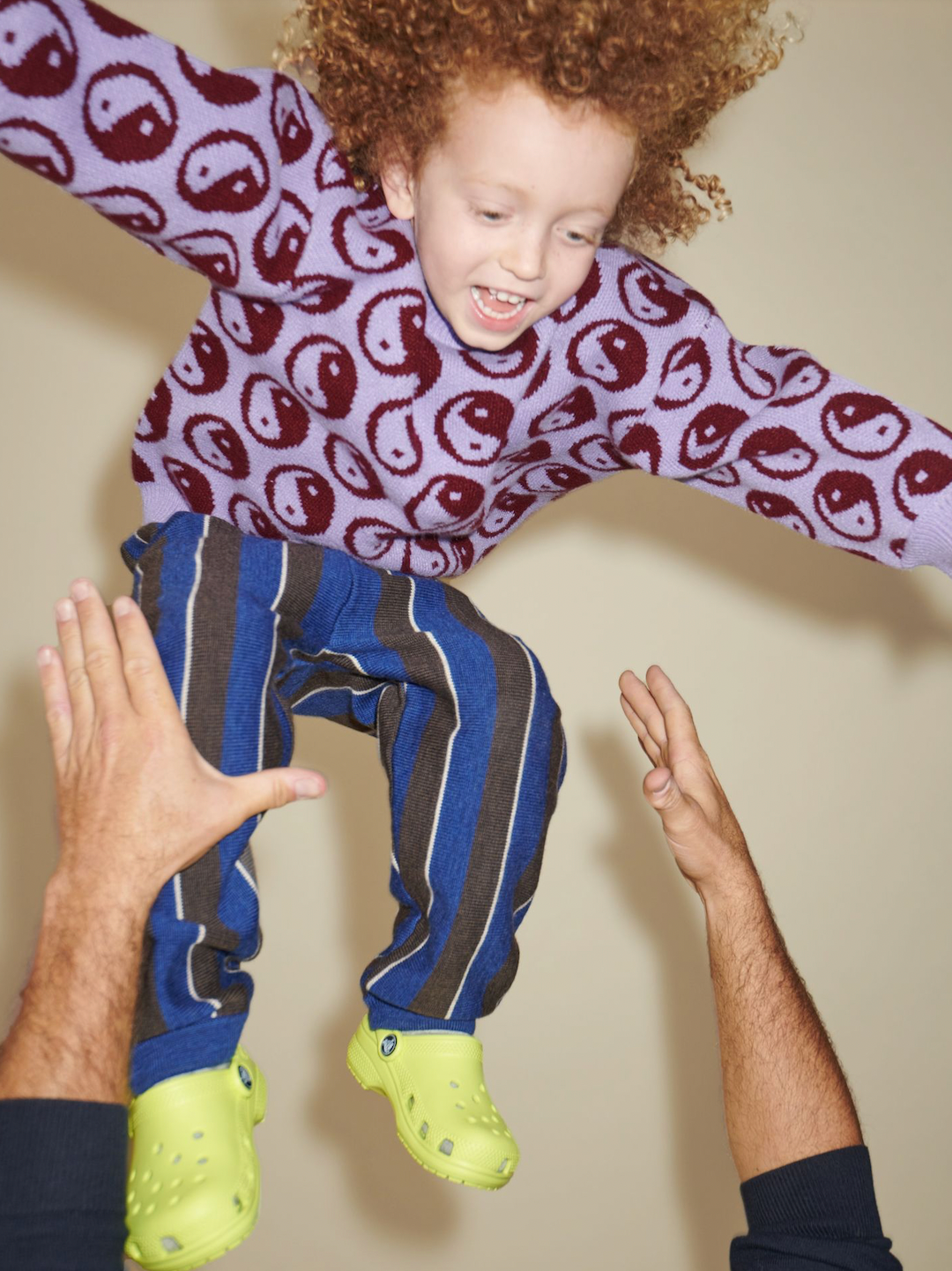 A laughing child being thrown in the air wearing a kids' sweater of dark red yin and yang circles on a violet background