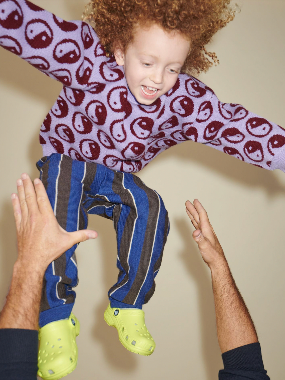 Violet | A laughing child being thrown in the air wearing a kids' sweater of dark red yin and yang circles on a violet background