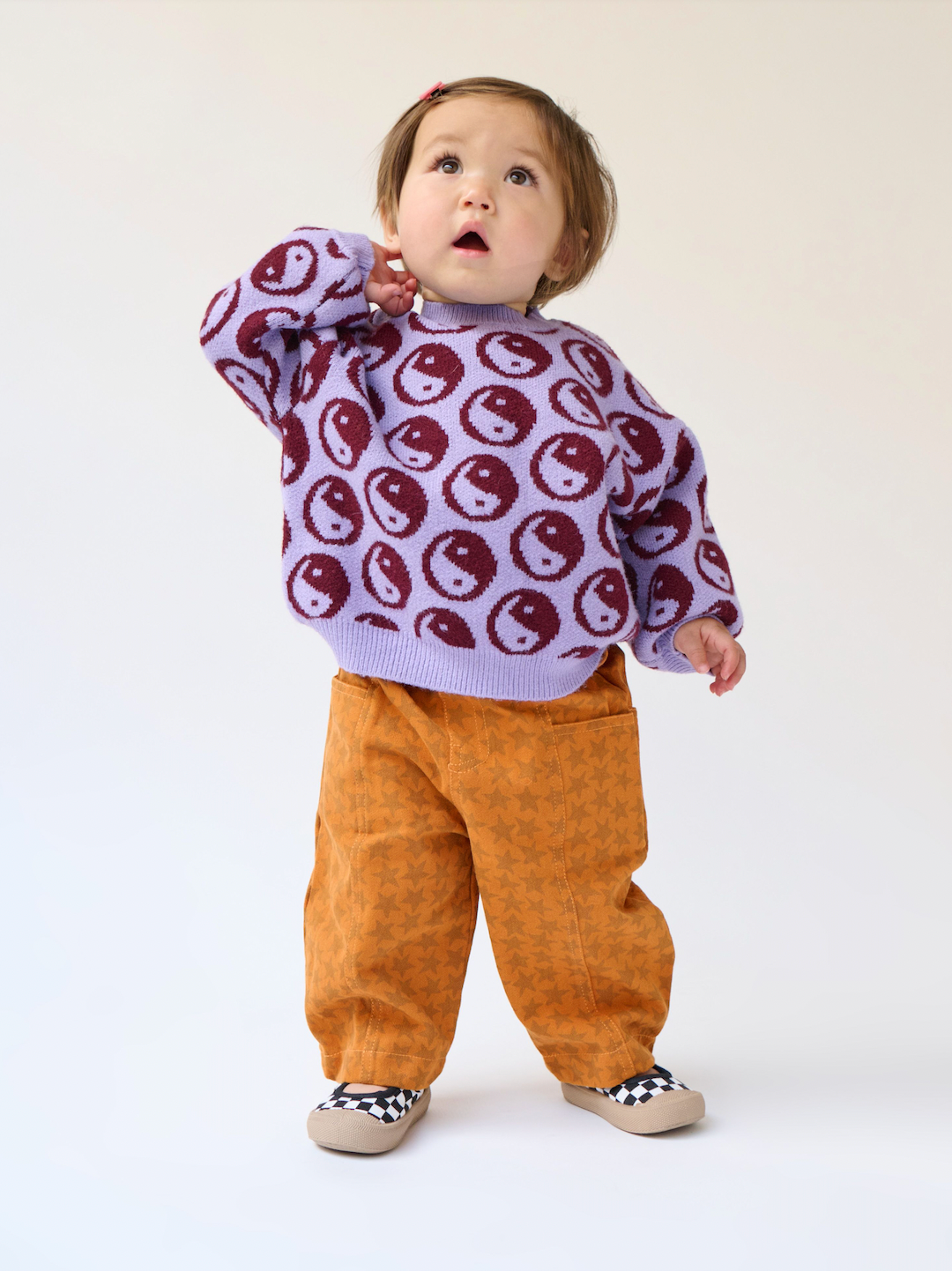 A toddler wearing a kid's sweater patterned with dark red yin and yang circles on a violet background