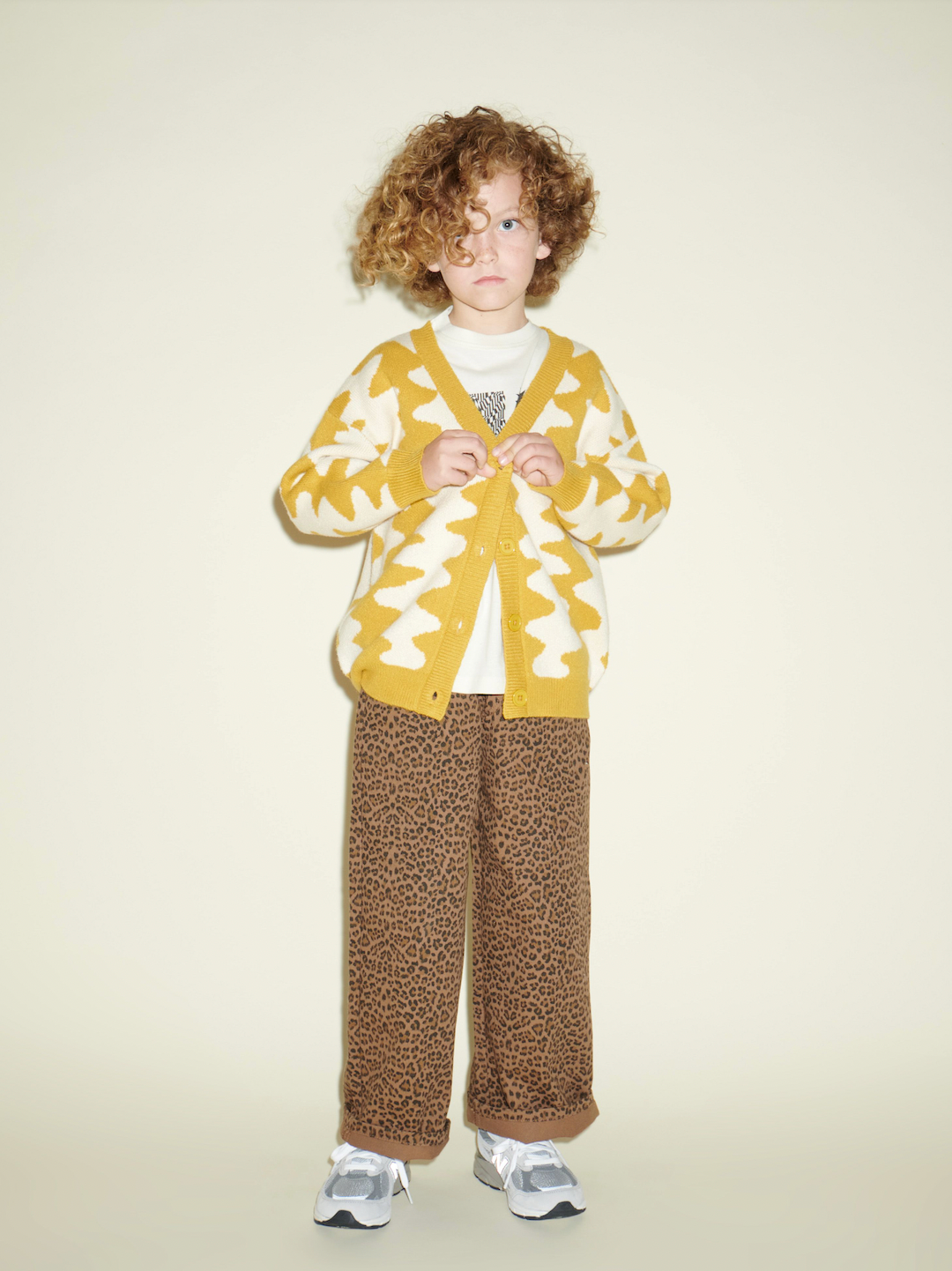 Marigold | A child wearing Marigold Wavelength Cardigan, with cheetah pants & sneakers, buttoning the sweater.