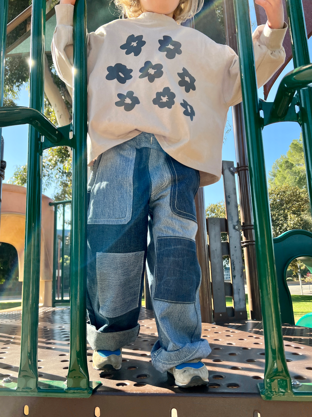 A child on a jungle gym wearing a kids' tee shirt in soft gray with dark gray flowers, over two-tone denim pants