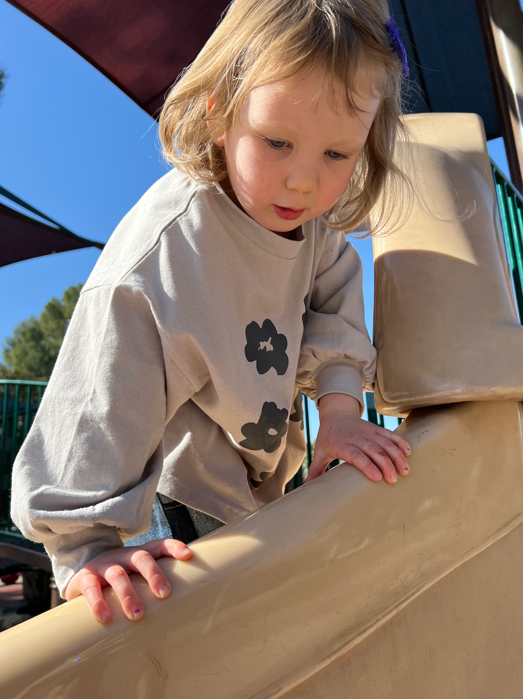 A child climbing on a jungle gym wearing a kids' tee shirt in soft gray with dark gray flowers, sleeves gathered at the cuffs