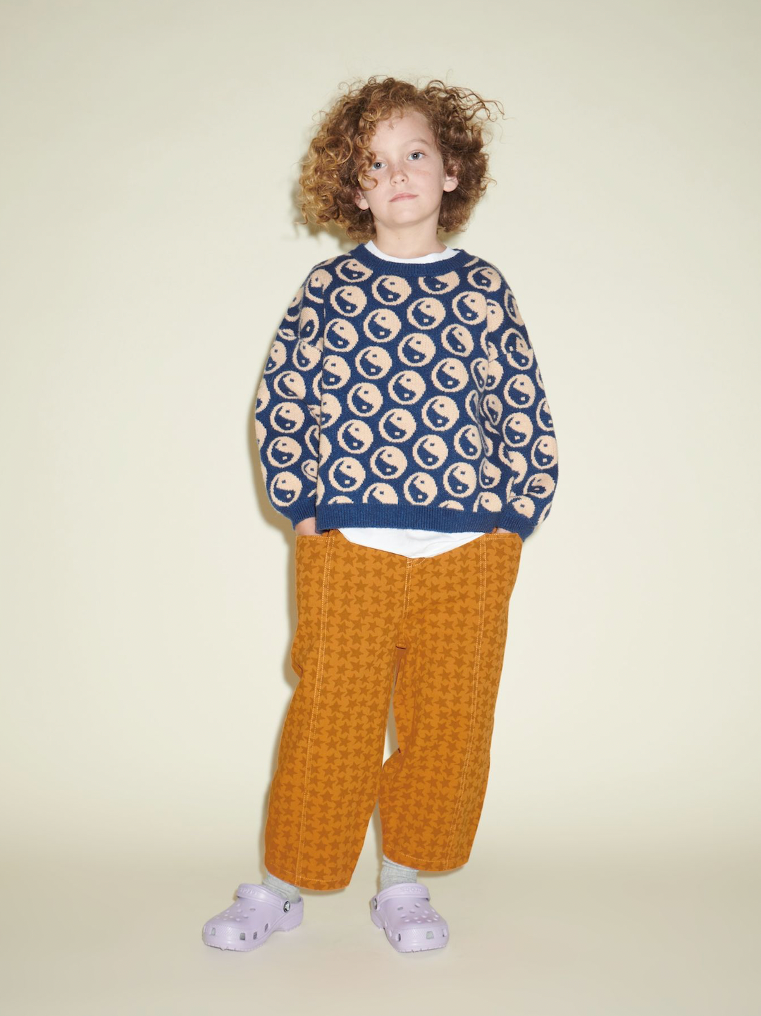 A child wearing a pair of kids' pants in an orange and rust star pattern, under a Cosmos Sweater in navy