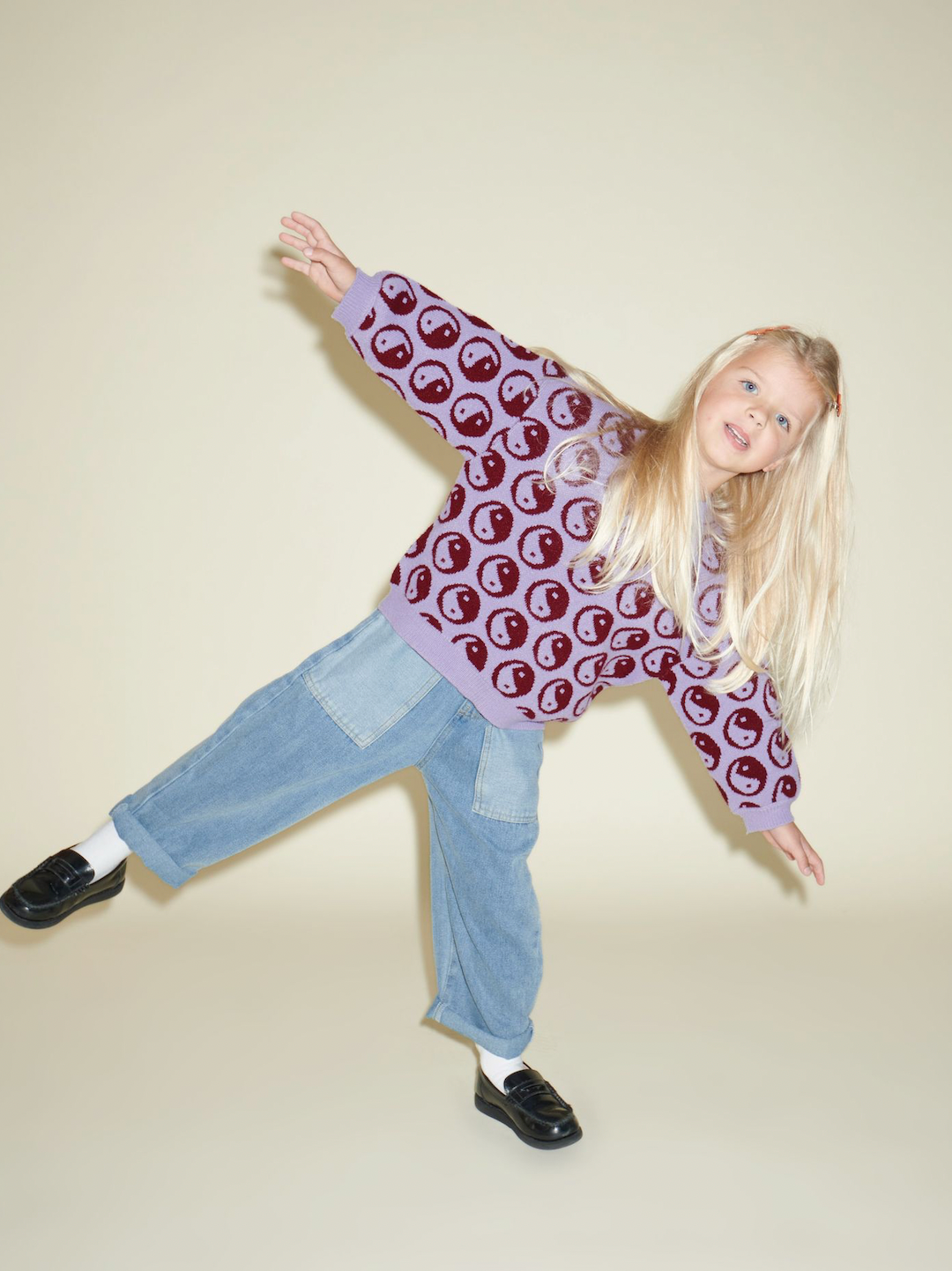 Violet | A child wearing a kids' sweater with dark red yin and yang circles on a violet background