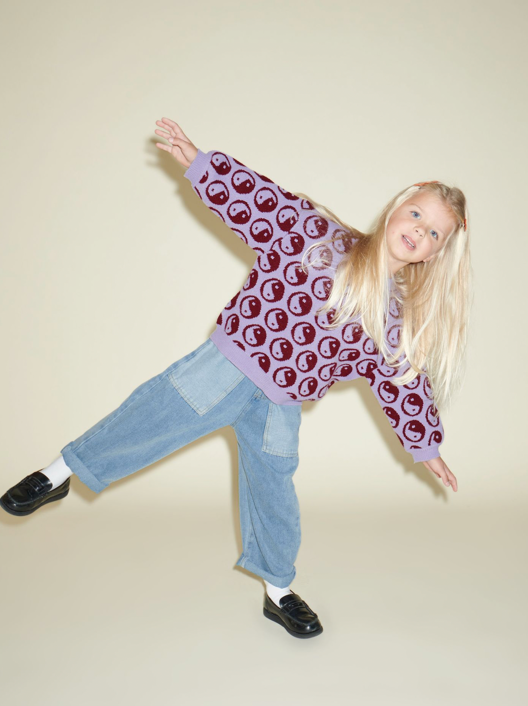 A child wearing a kids' sweater with dark red yin and yang circles on a violet background