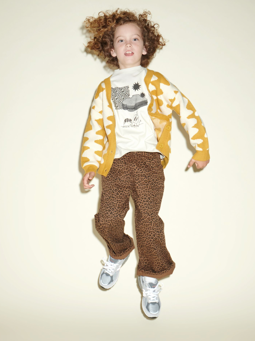 A child jumping in a cream and black Sandwich Tee under a Wavelength Cardigan in marigold