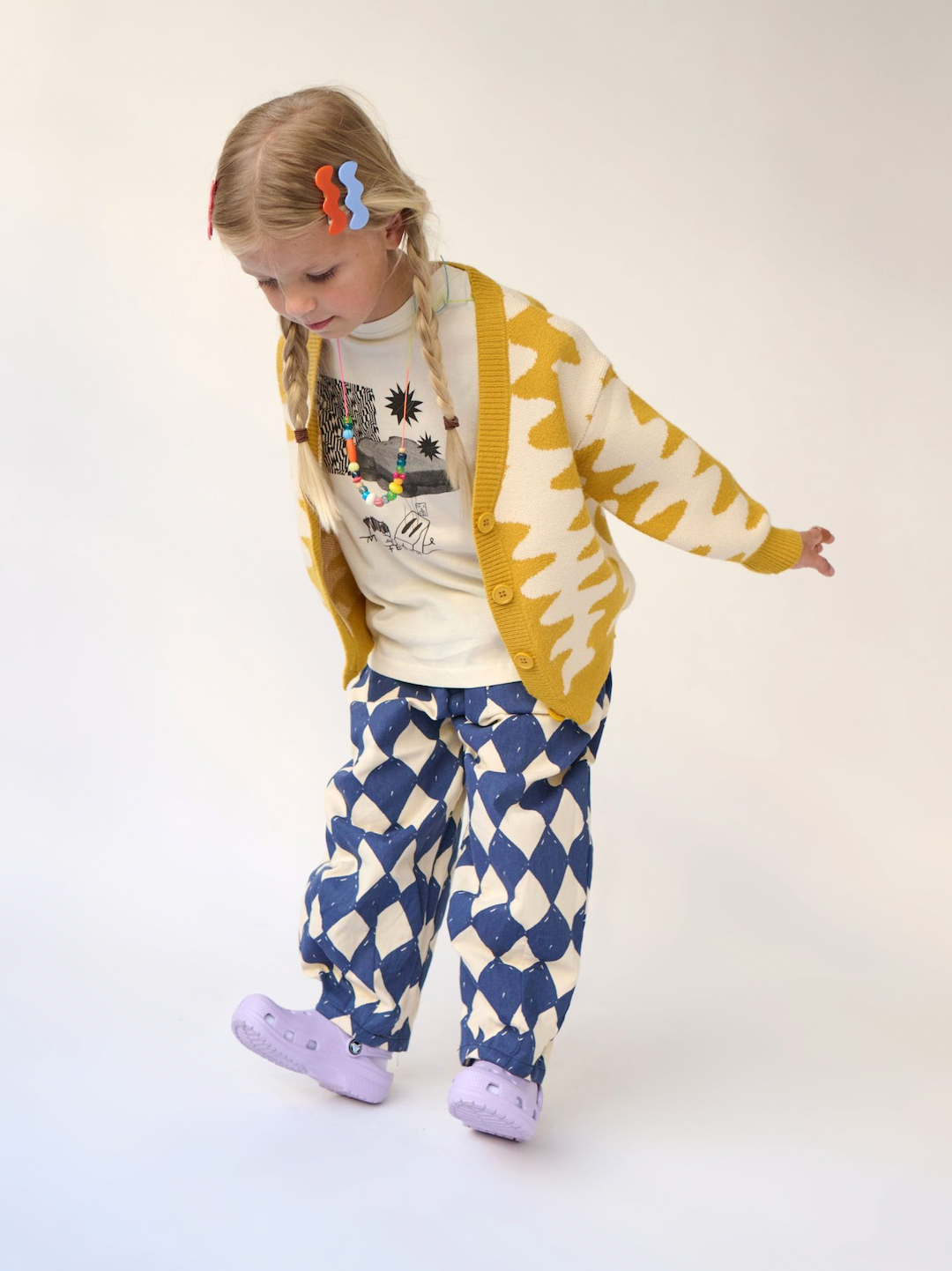 A child wearing a cream and black Sandwich Tee under a Wavelength Cardigan in marigold
