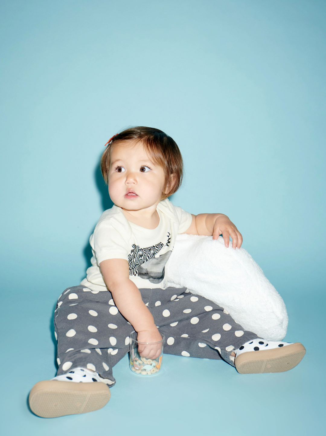 A toddler sitting with a pair of mary jane sneakers with black dots on a white background