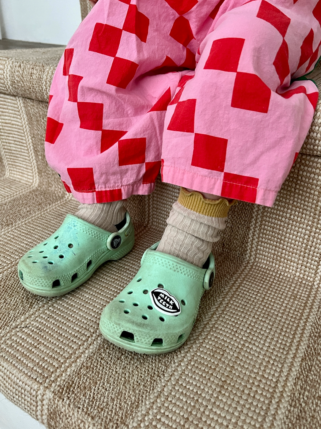 A child wearing pale green Crocs with a Milk Teeth charm