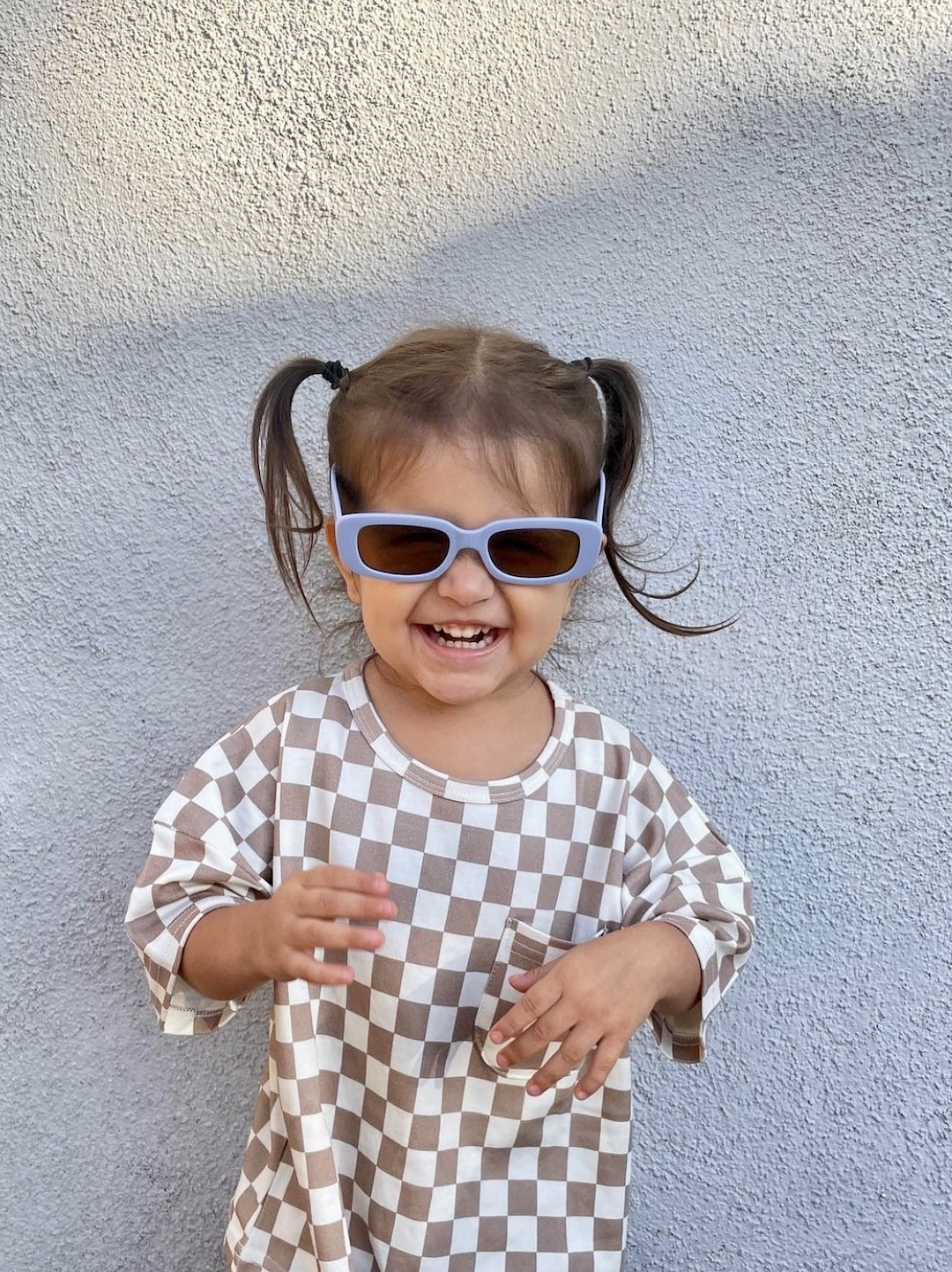 A smiling child wearing a pair of kids' sunglasses with brown lenses inside pale blue frames